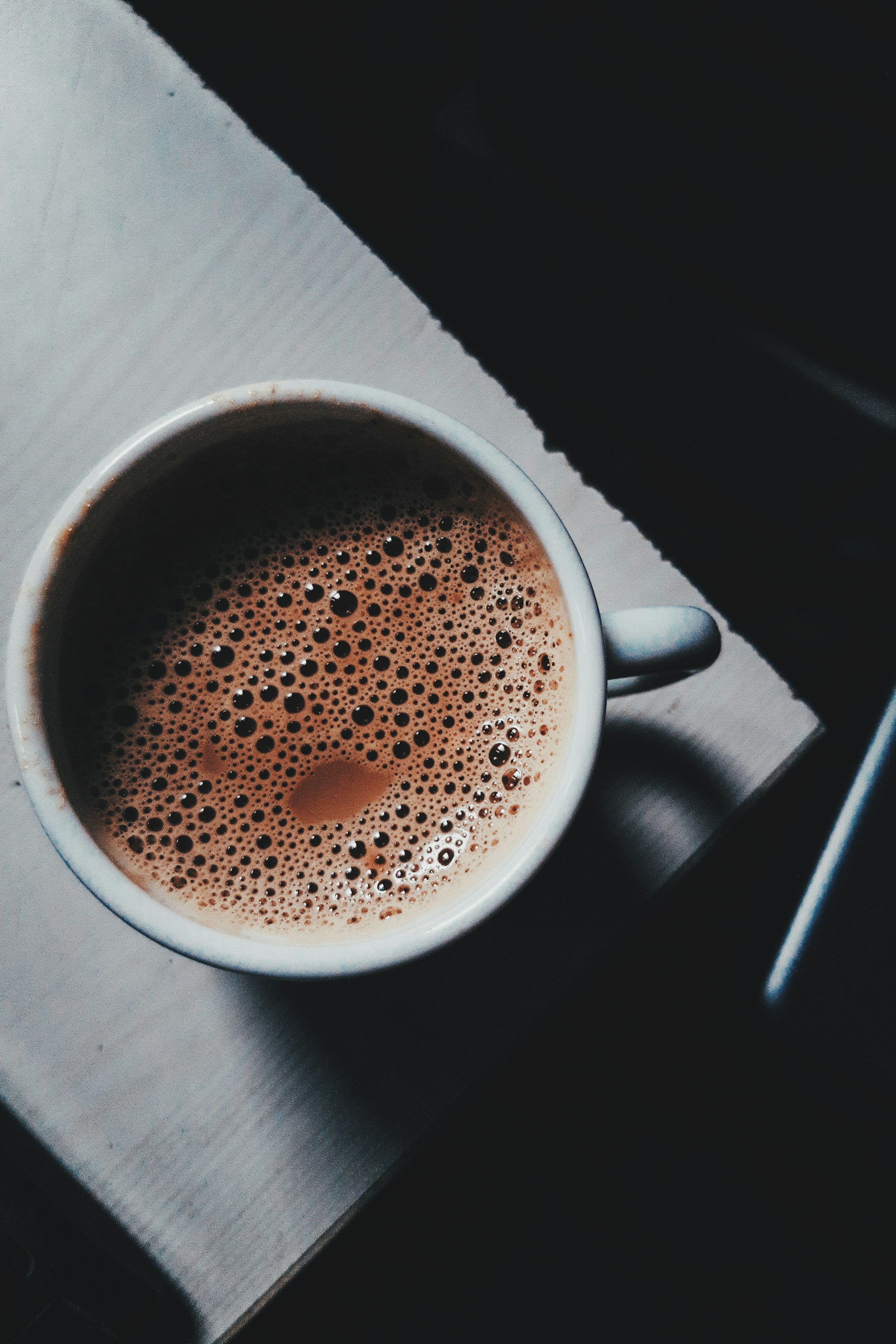An inviting shot of a rich, frothy coffee served in a rustic ceramic cup, resting on a wooden table with soft morning light.