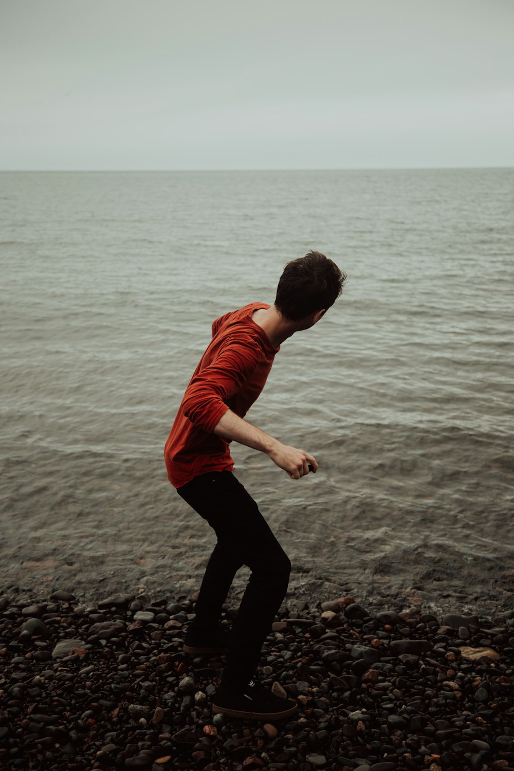 man wearing red shirt about to throw stone on ocean