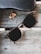 A pair of dark sunglasses rests on a worn wooden surface. Near the sunglasses, there is a small, dried leaf. A black, textured eyeglass case also lies on the surface.