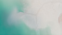 Aerial view of a coastline where vibrant turquoise waters meet a sandy, white shore. The blending of colors creates a serene atmosphere with soft gradients and smooth textures.