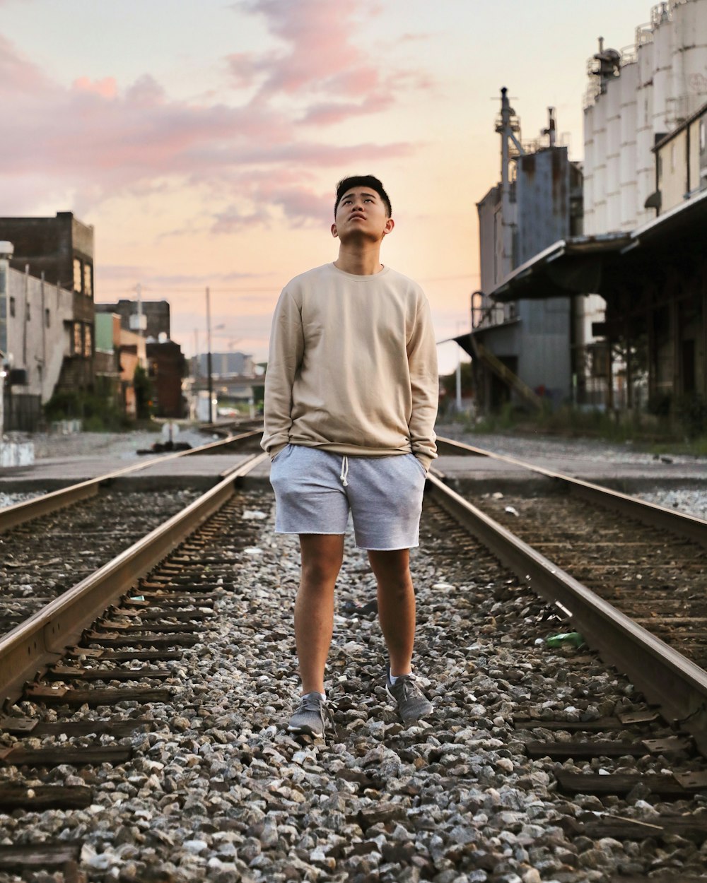 man wearing gray sweater standing on railway looking up