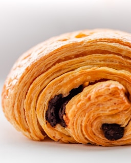 A close-up of a golden-brown pain au chocolat with melted chocolate peeking out.