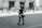 A bronze statue of a young girl with her hands on her hips stands confidently on a cobblestone street. She faces a building with ornate architecture and closed shutters, separated by a black iron fence. The image conveys a sense of empowerment through the girl's determined stance.
