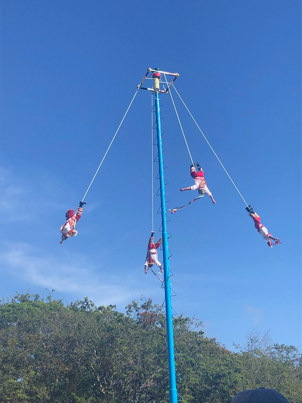 four acrobats dangling from blue pole