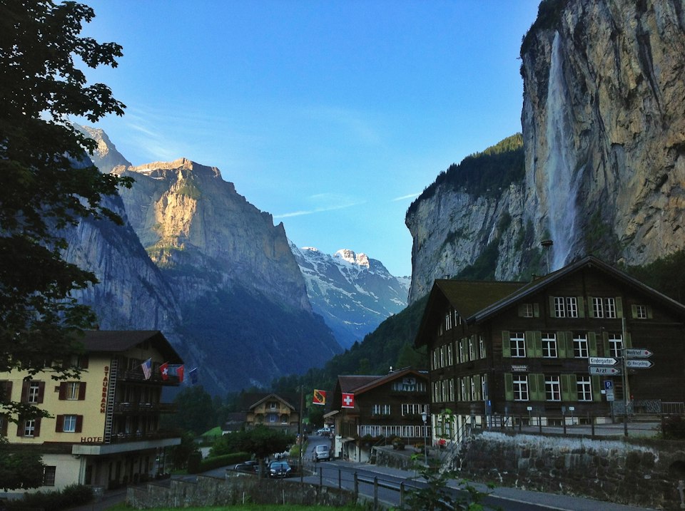 A quiet Lauterbrunnen street at dusk with wooden chalets and Staubbach Falls dropping down the cliffside behind the village