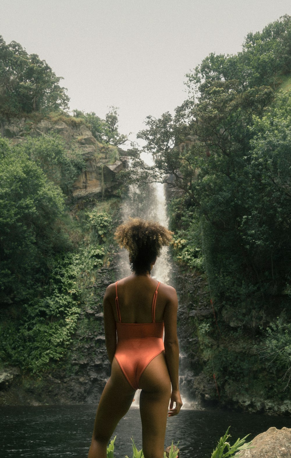 Frau trägt orangefarbenen Badeanzug mit Blick auf Wasserfälle