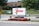 A sign stands prominently near the road, displaying 'US Lacrosse' in large red letters above a logo, and below it reads 'MedStar Health' along with an address '2 Loveton Circle'. The sign is surrounded by well-maintained landscaping, featuring red flowers and neatly trimmed grass. In the background, there is a building with a brick facade, trees, and additional signage, indicating a peaceful, suburban setting.
