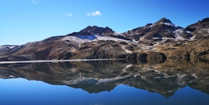 A cinematic 4k image of a snow-capped mountain peak under a clear blue sky, reflected perfectly in a dark, still lake.