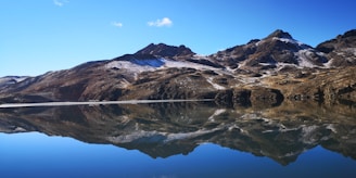 A cinematic 4k image of a snow-capped mountain peak under a clear blue sky, reflected perfectly in a dark, still lake.