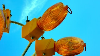 Several orange construction lights attached to square yellow bases are mounted on a white pole against a bright blue sky.
