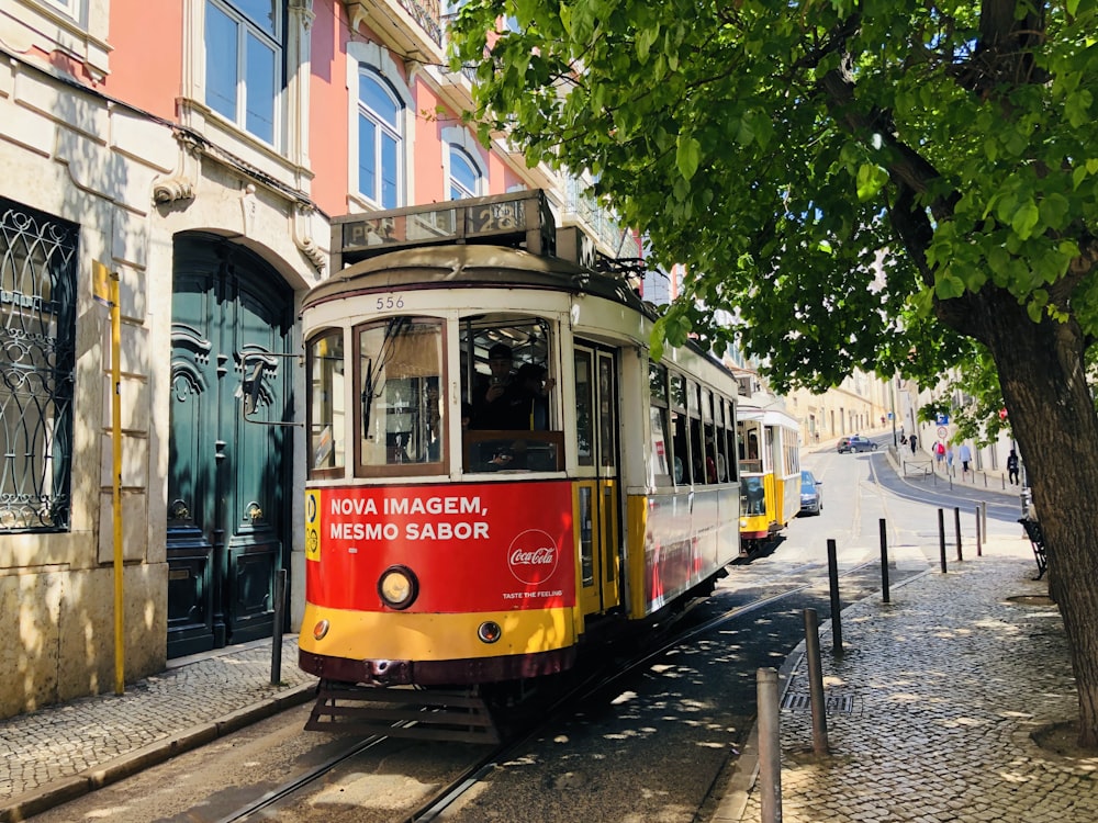 white and red train on rail between tree and building