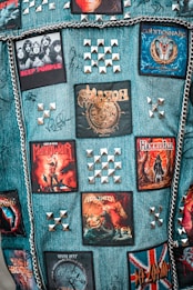 A denim vest adorned with band patches, metal studs, and chains. The patches feature rock and metal bands such as Deep Purple, Saxon, Whitesnake, Manowar, and Helloween. Metal pyramid studs are arranged in patterns around the patches.