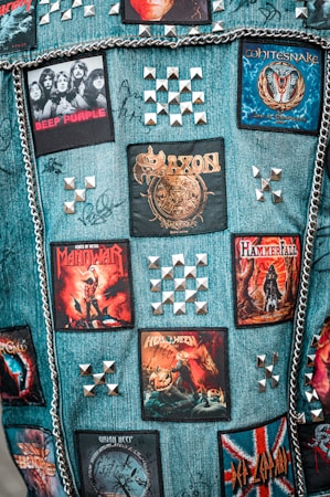 A denim vest adorned with band patches, metal studs, and chains. The patches feature rock and metal bands such as Deep Purple, Saxon, Whitesnake, Manowar, and Helloween. Metal pyramid studs are arranged in patterns around the patches.