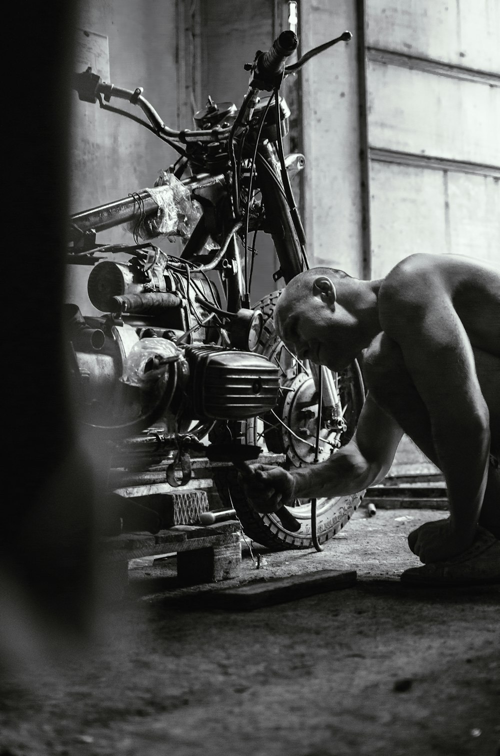 grayscale photography of man fixing motorcycle