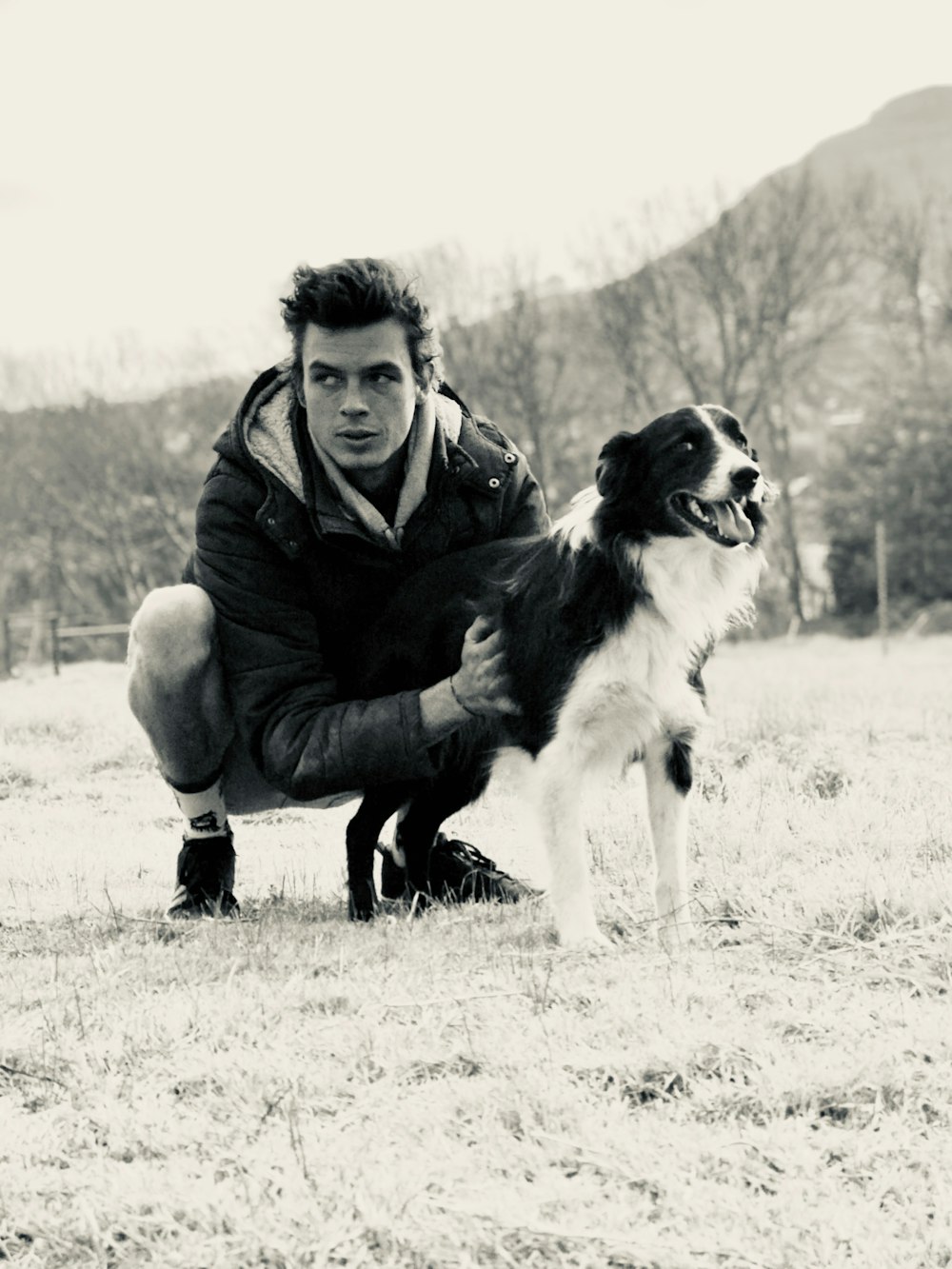 낮 동안 야외 근처에서 개를 안고 있는 남자의 회색조 사진