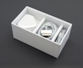 A neatly arranged white box containing a power adapter, a coiled charging cable, and an audio cable. The box is sectioned into compartments, neatly organizing the electronic accessories.