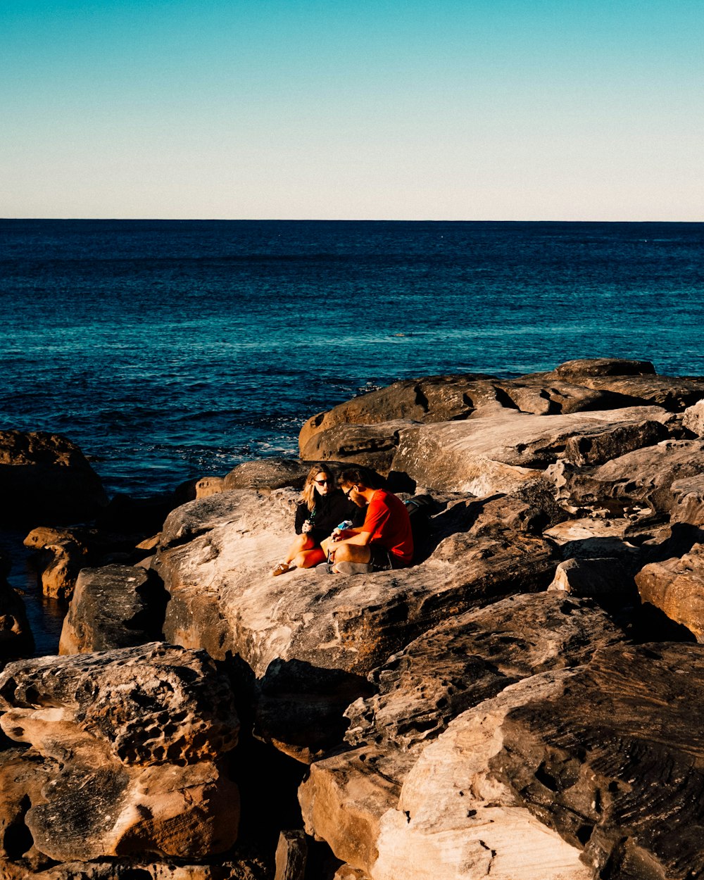 man and woman sitting on rock near ocean