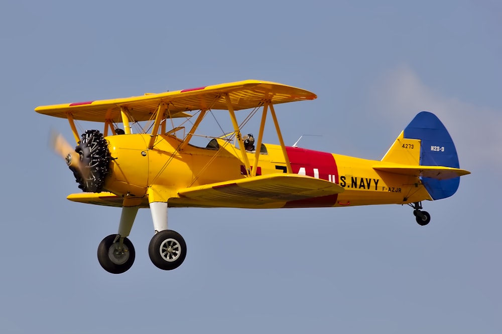 Biplano giallo, rosso e blu che vola sotto il cielo blu