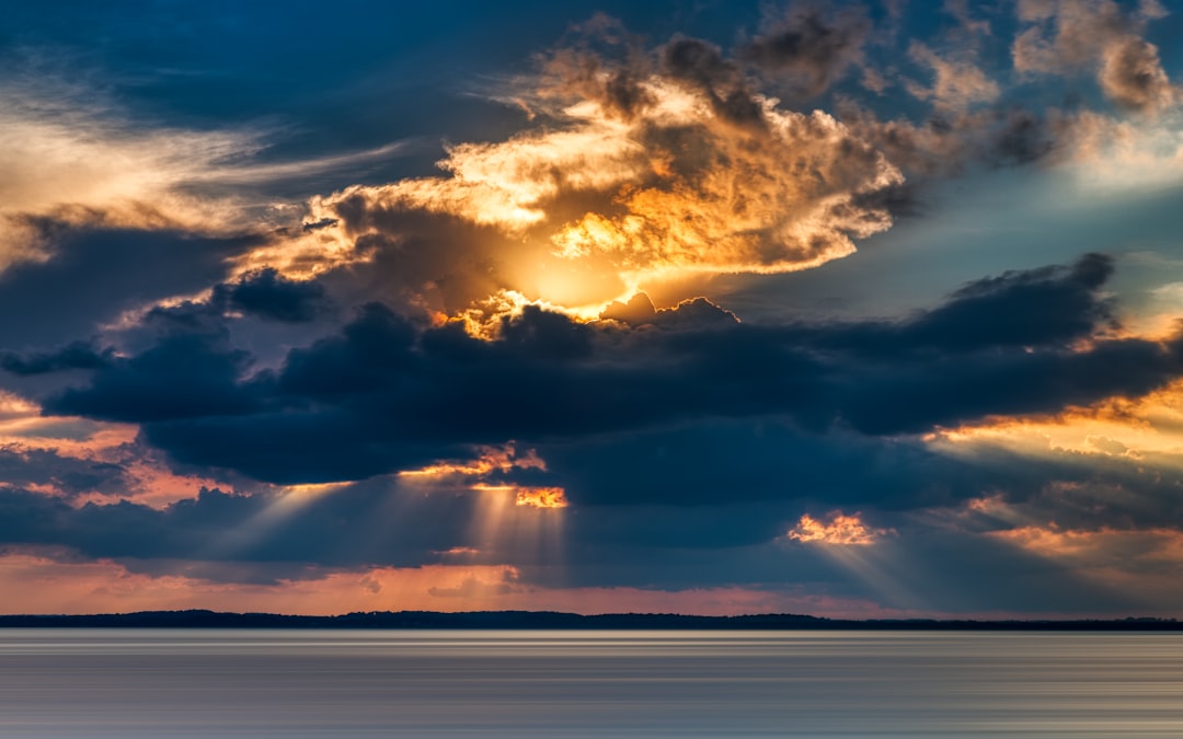 crepuscular photography of rays from cumulus clouds into the sea