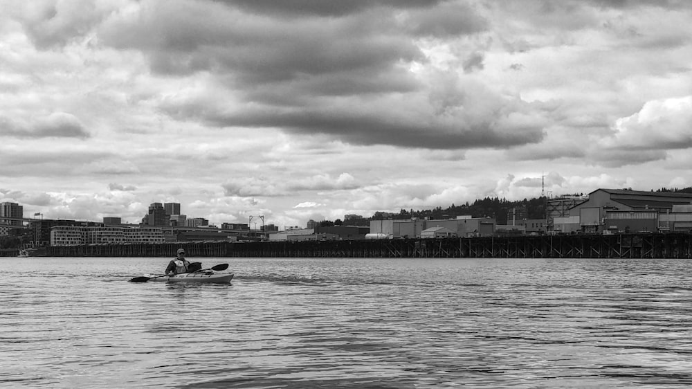grayscale photography of man riding boat on body of water and cityscape