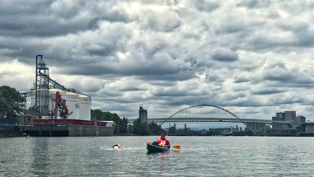 man kayaking on sea viewing bridge under white and gray skies