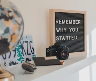 shallow focus photo of black SLR camera on white wooden shelf