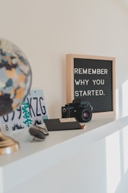 shallow focus photo of black SLR camera on white wooden shelf