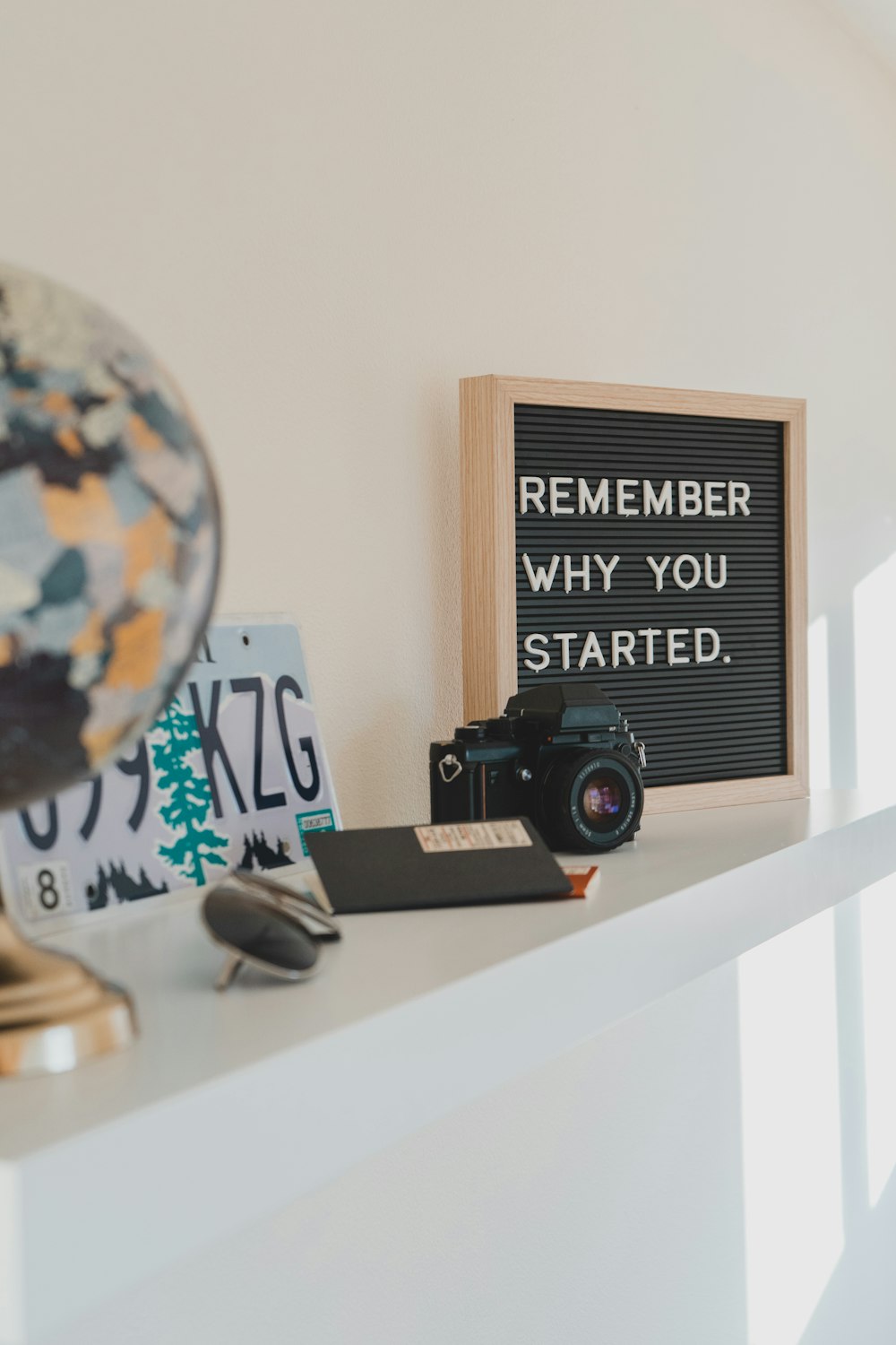 shallow focus photo of black SLR camera on white wooden shelf with a sign reading "remember why you started"