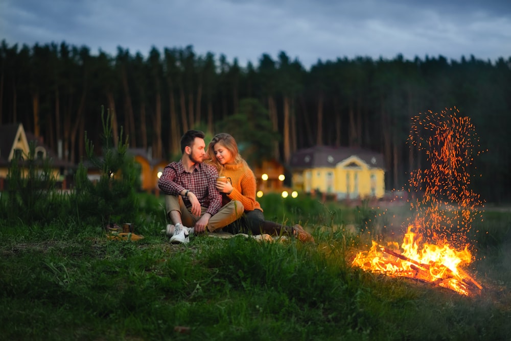 shallow focus photo of man and woman sitting on grass beside fire pit