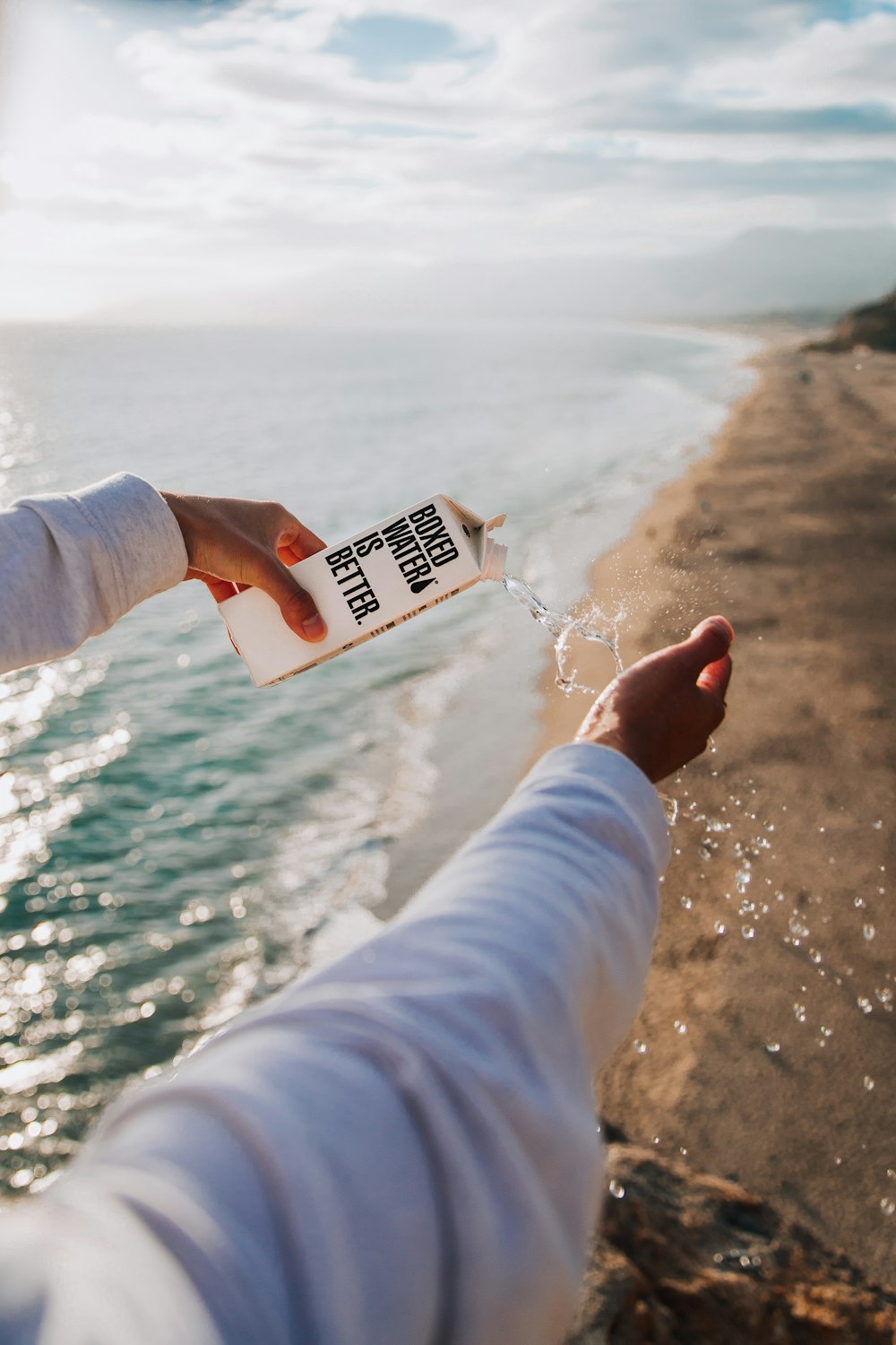 person holding boxed water across seashore