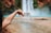 A hand is pouring water from a carton labeled 'Boxed Water is Better' in front of a blurred waterfall with a pool at the base. The background consists of a natural landscape with water and rugged terrain.