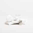 A white, sleek container with the brand name 'Candid', a small bottle labeled 'Whitener', and a clear dental aligner rest on marble slabs. The composition is minimalist with an emphasis on dental care products.