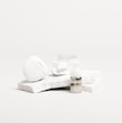 A white, sleek container with the brand name 'Candid', a small bottle labeled 'Whitener', and a clear dental aligner rest on marble slabs. The composition is minimalist with an emphasis on dental care products.
