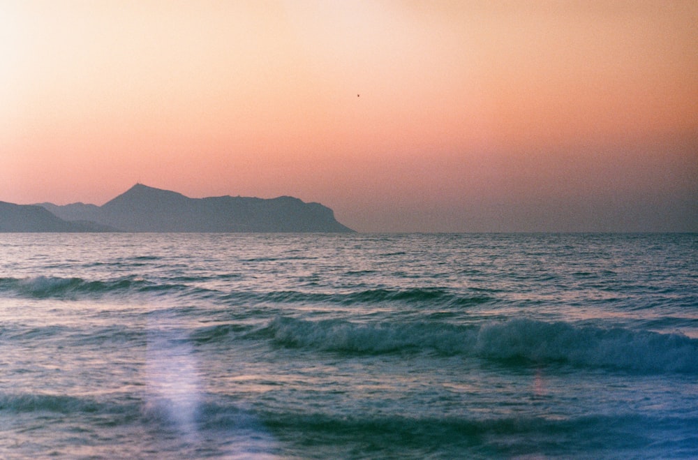 the sun is setting over the ocean with mountains in the distance