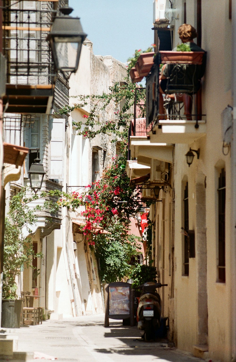 a narrow city street with flowers on the balconies