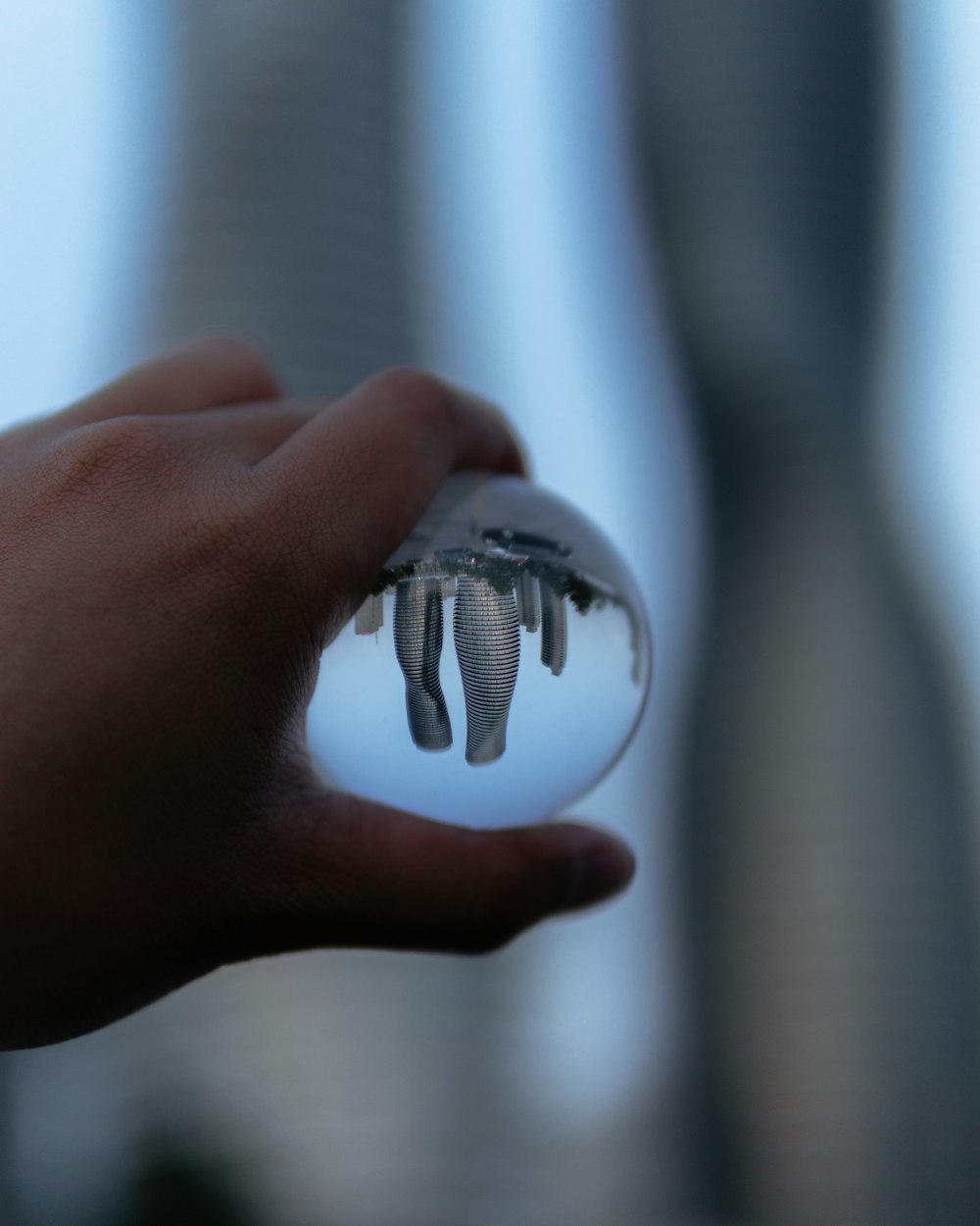 person holding clear glass ball with reflection of city