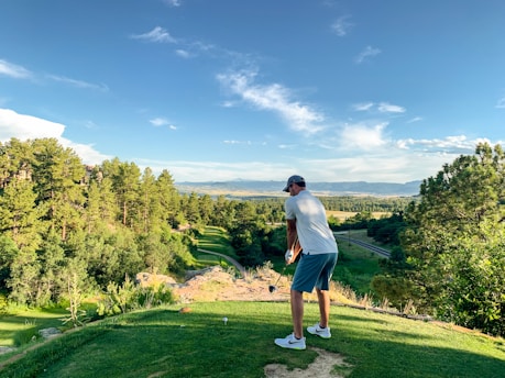 A golfer practicing their swing on a lush green driving range under a clear blue sky.