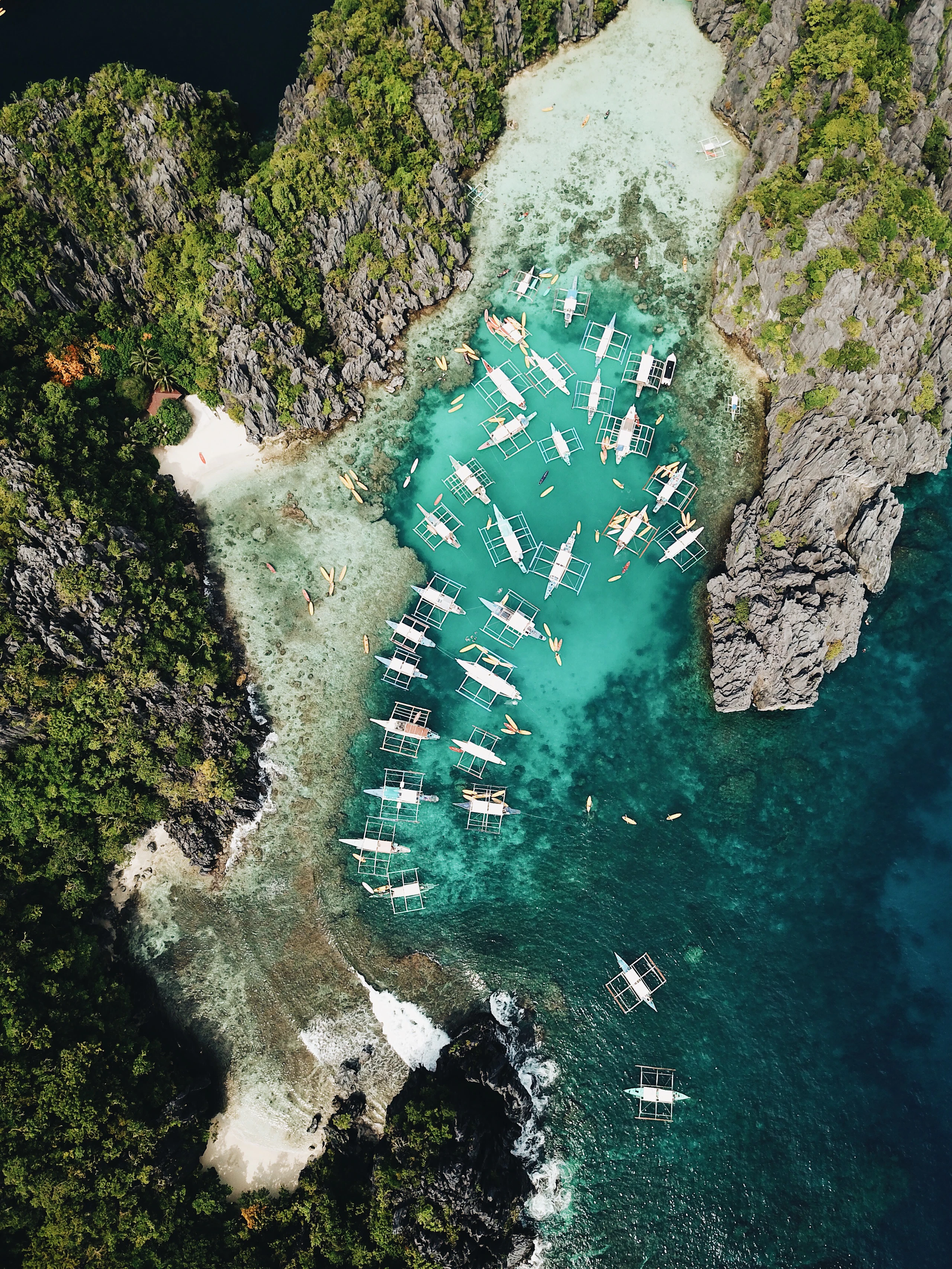A wooden outrigger boat at anchor in a green lagoon below limestone cliffs, El Nido