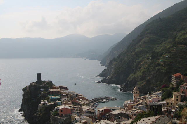 Vernazza seen from the coastal trail above, its harbor and watchtower on the point below hazy hills