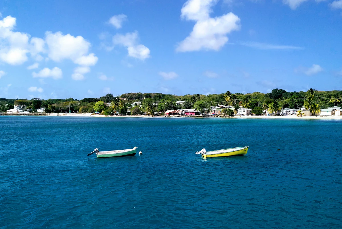 Small boats anchored in a calm bay near Colleton, Barbados, with houses along the shoreline, representing the island's maritime industry