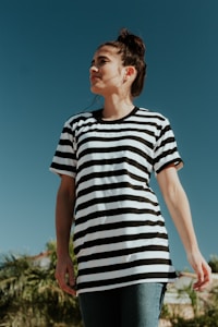 A person is wearing a black and white striped shirt with the word 'freedom' printed on it. They are standing outdoors under a clear blue sky, looking upwards with a calm expression. There are palm trees in the background.