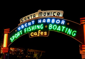 A brightly lit, colorful neon sign with the words 'Santa Monica Yacht Harbor Sport Fishing Boating Cafes' against a dark background.