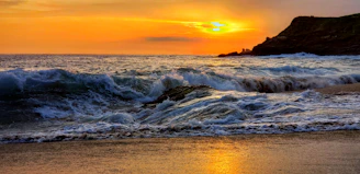 A vibrant sunset over the volcanic coastline of the Canary Islands with waves crashing gently on the shore.