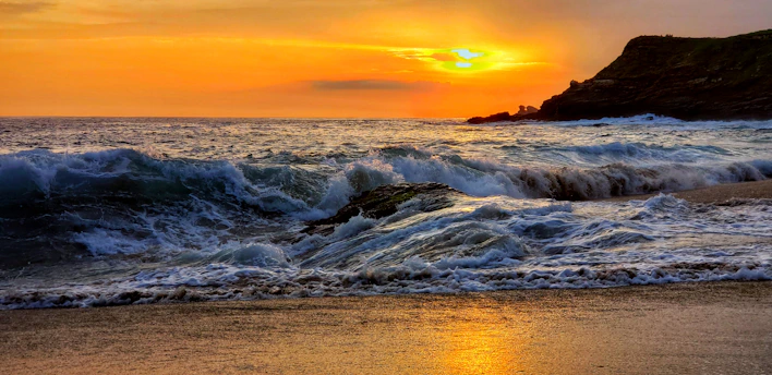 A vibrant sunset over the volcanic coastline of the Canary Islands with waves crashing gently on the shore.