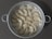 A round metal steamer filled with several steamed dumplings arranged neatly. The dumplings have a glossy, slightly translucent appearance, indicating they are freshly cooked. The steamer has two handles, and the background features a textured, dark surface.