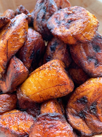 Golden-brown fried plantain slices showing a crispy exterior and slightly charred edges, with a glossy texture indicating freshness and a deliciously caramelized finish.