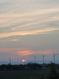 Wind turbines spinning over open fields at sunset