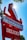 A red and white retro-style sign displays advertisements for hamburgers, emphasizing 'Instant Service' and 'Dick's Deluxe 1/4 lb. 100% Beef.' The sign is set against a clear blue sky with sunlight creating a starburst effect.