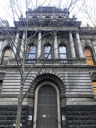 An old, grand university building with large columns and arched windows. The architecture is adorned with intricate stonework and a prominent entrance under bare tree branches.