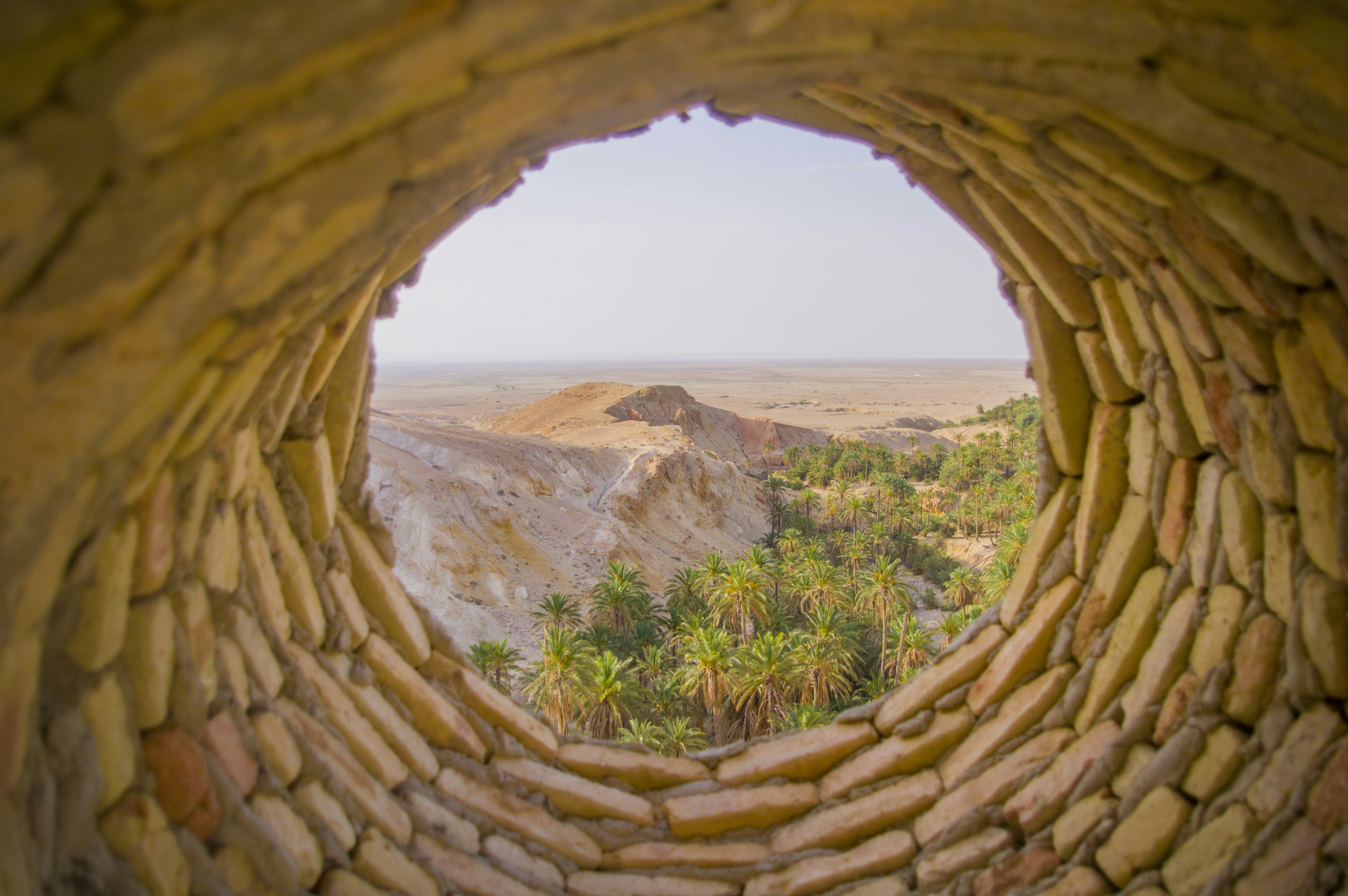 a view of a desert through a hole in a rock wall, 